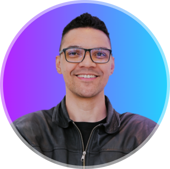  Foto de Mayk Brito sorrindo, usando óculos e camisa preta, barba e fundo neon. 